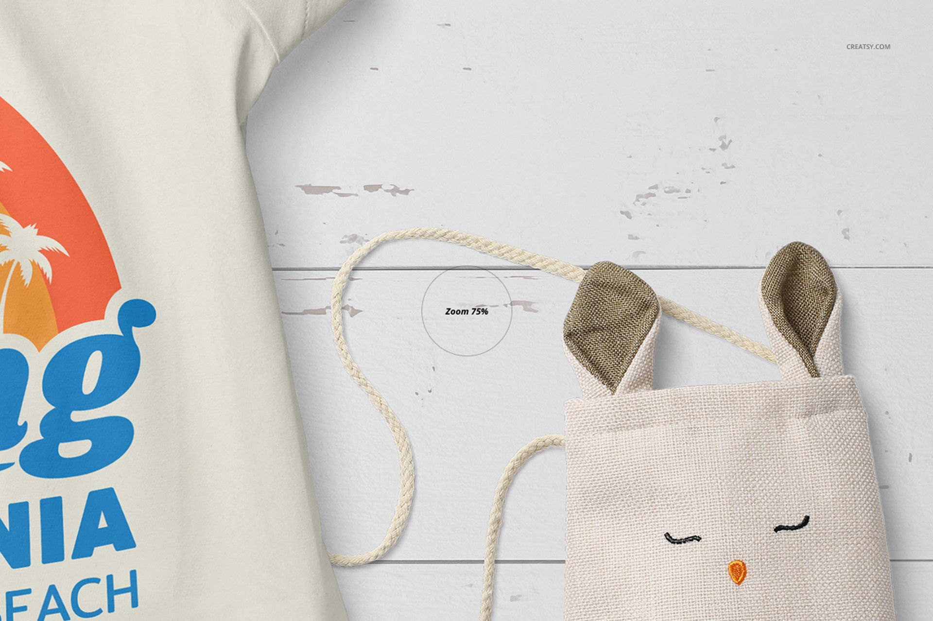 Front view of a baby summer set mockup showing part of a cream-colored t-shirt with a colorful print and a small fabric bag with bunny ears on a white wooden surface.