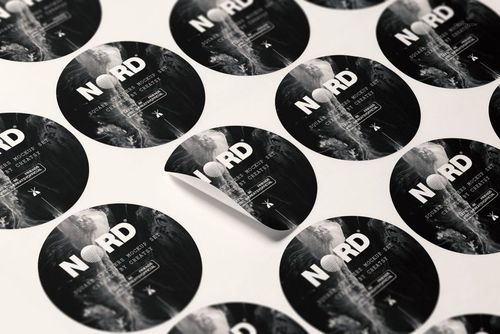 Round stickers with monochrome abstract designs arranged on a flat surface, one sticker partially peeled up.