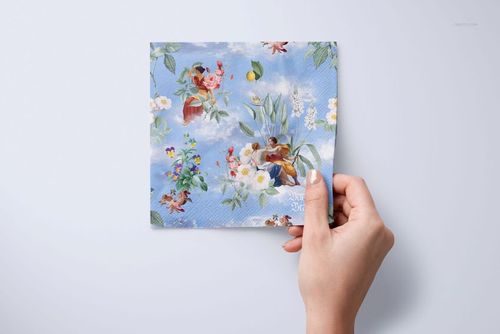 Square napkin mockup with a vibrant floral and sky design, displayed in a hand against a neutral backdrop.