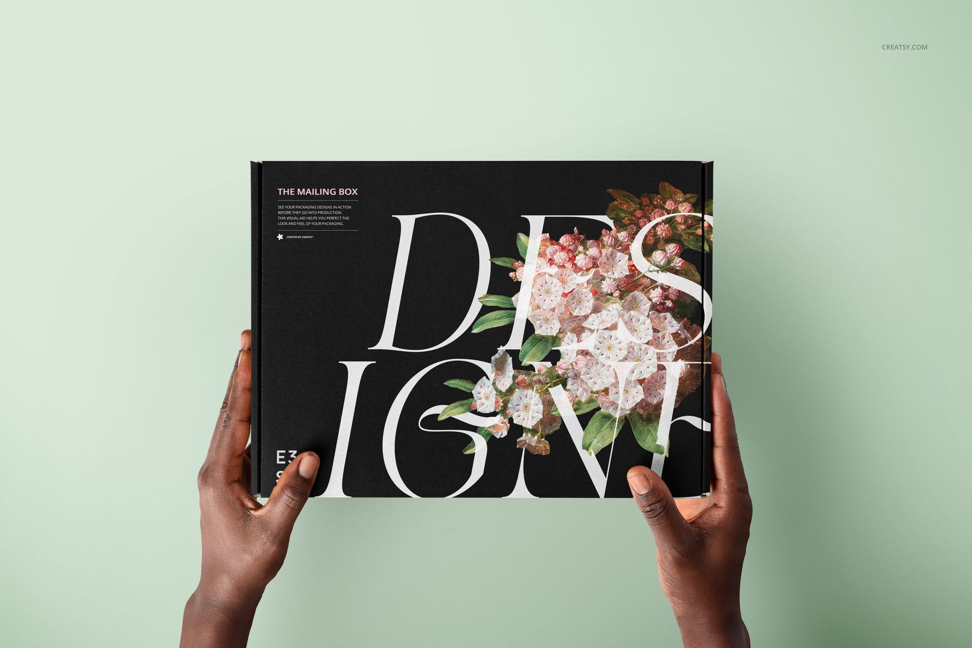 Mailing box mockup held in two hands, featuring a black surface with floral design and large white text.