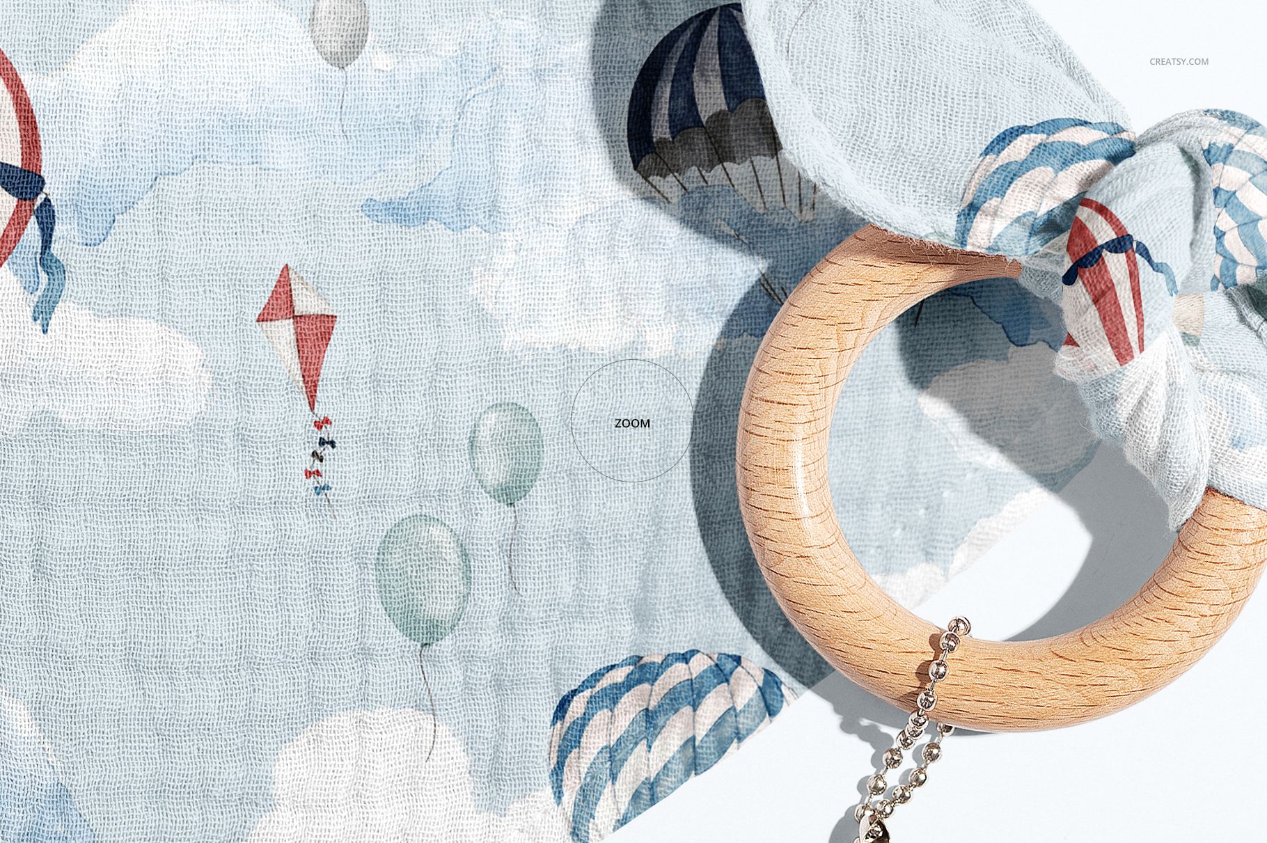 Detailed view of a baby muslin bandana mockup, showing blue and white clouds, hot air balloons, and a wooden teething ring.
