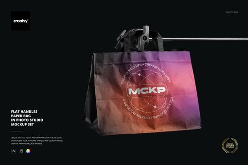 Flat handles paper bag mockup with gradient purple and orange design, hanging on a metal stand in a studio setting.