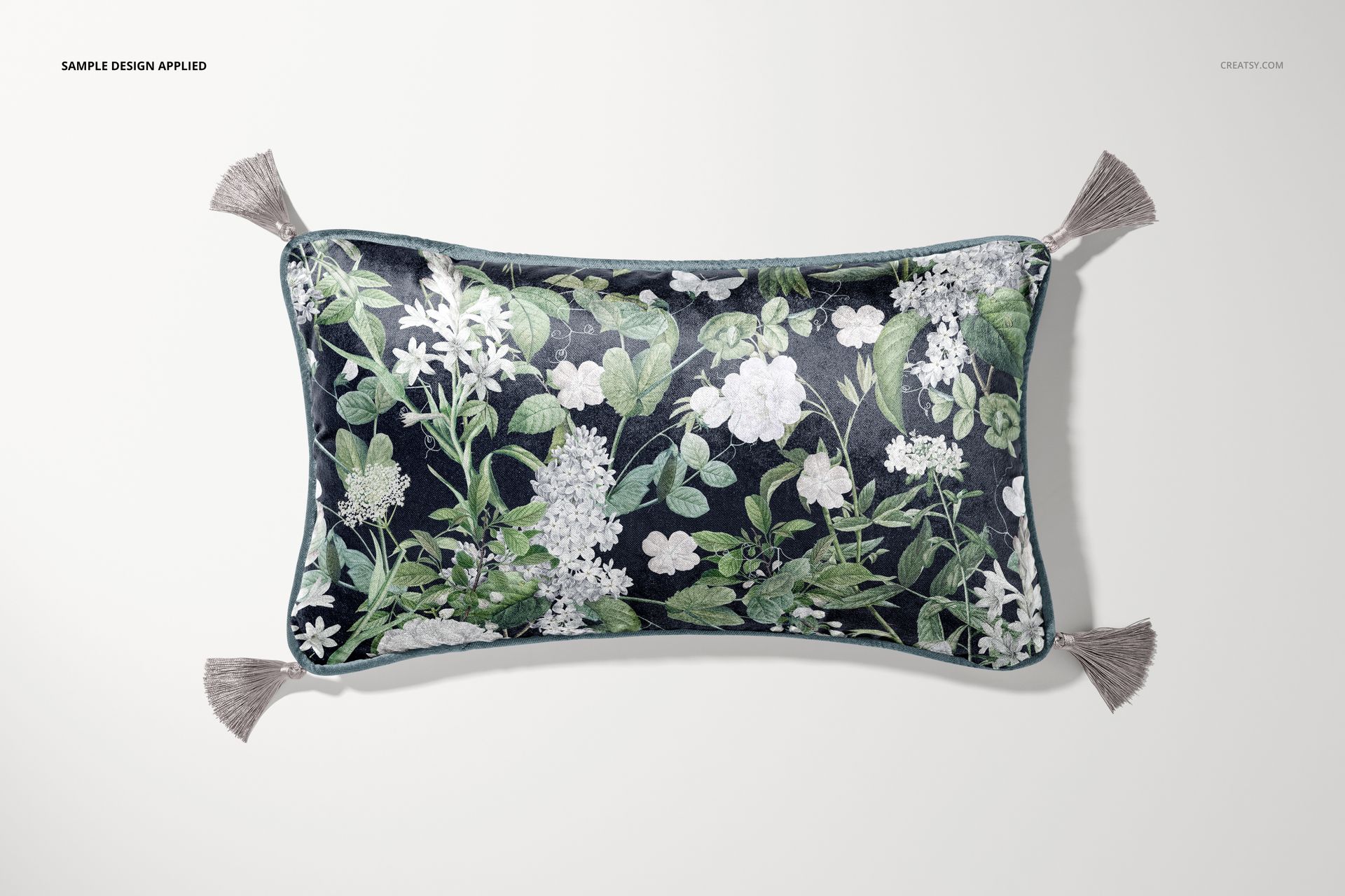 Velvet pillow mockup with tassels, displaying a botanical print in green and white, shown from above on a plain surface.