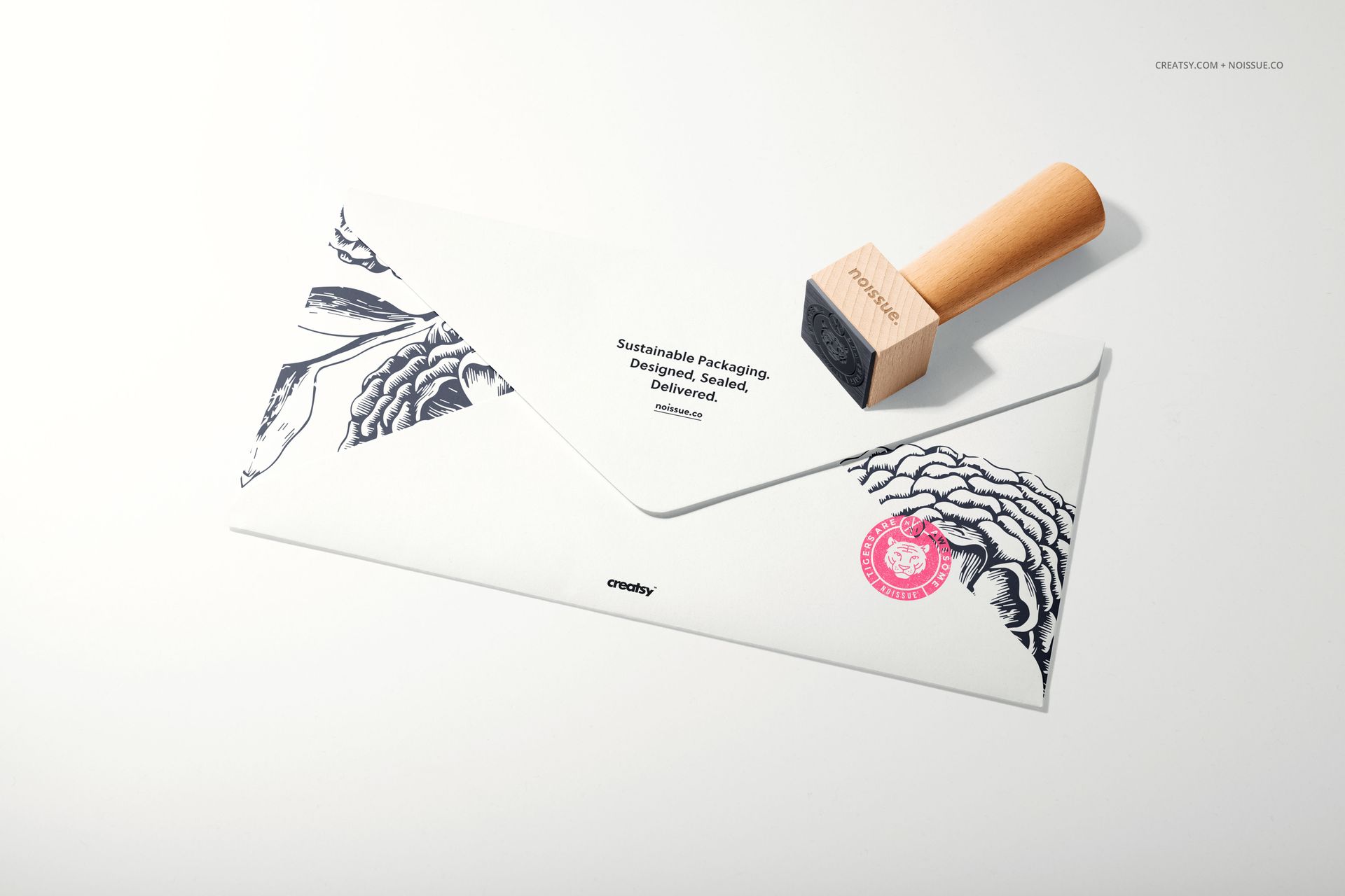 Stationery mockup showing a wooden stamp and envelope with monochrome designs and a pink seal on a light surface.