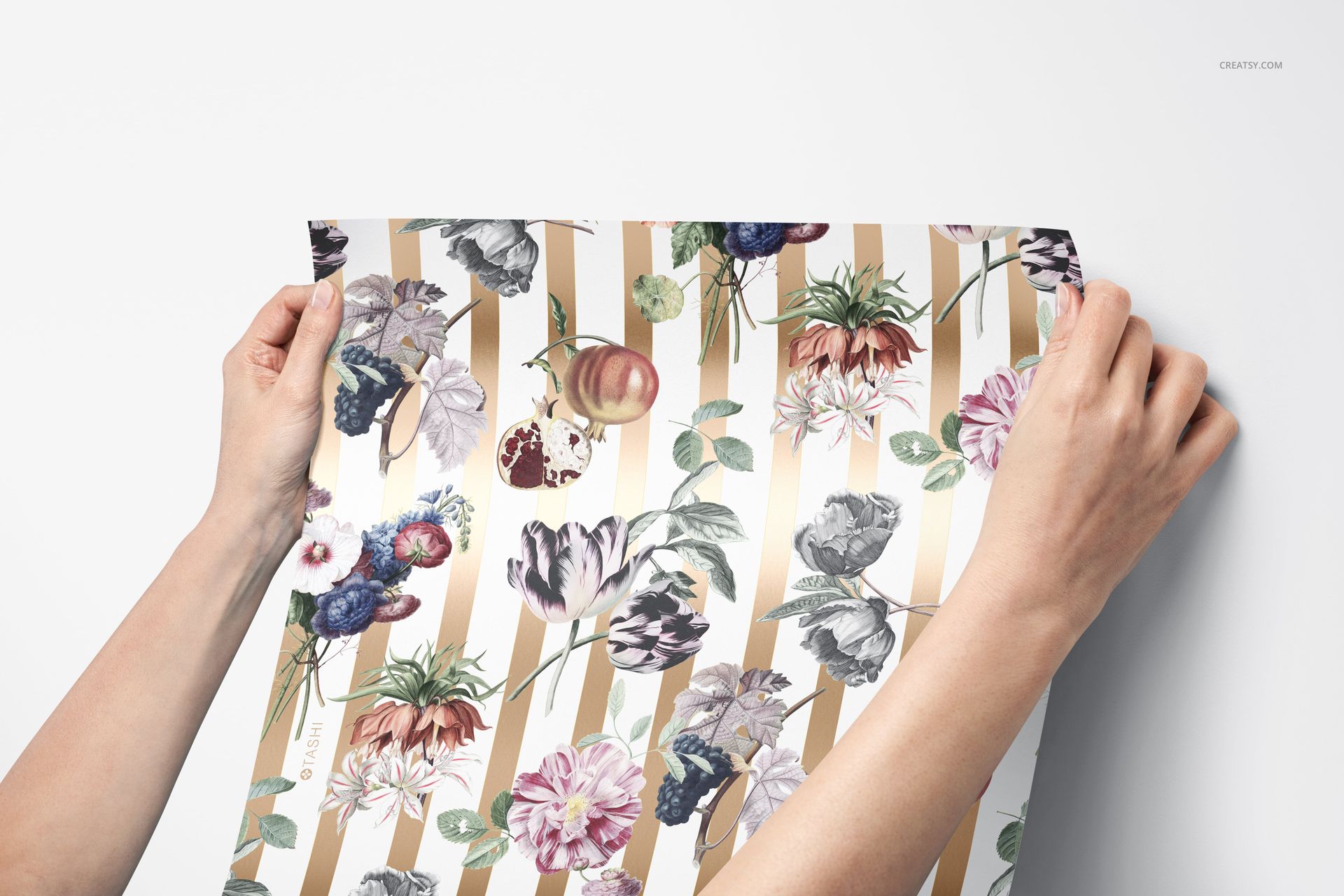 Person holding decorative wallpaper mockup featuring colorful flowers and gold stripes, shown from a top perspective.