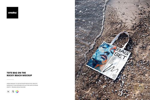 Tote bag with abstract blue and orange design lying on rocky beach near water, shown in a top view mockup scene.
