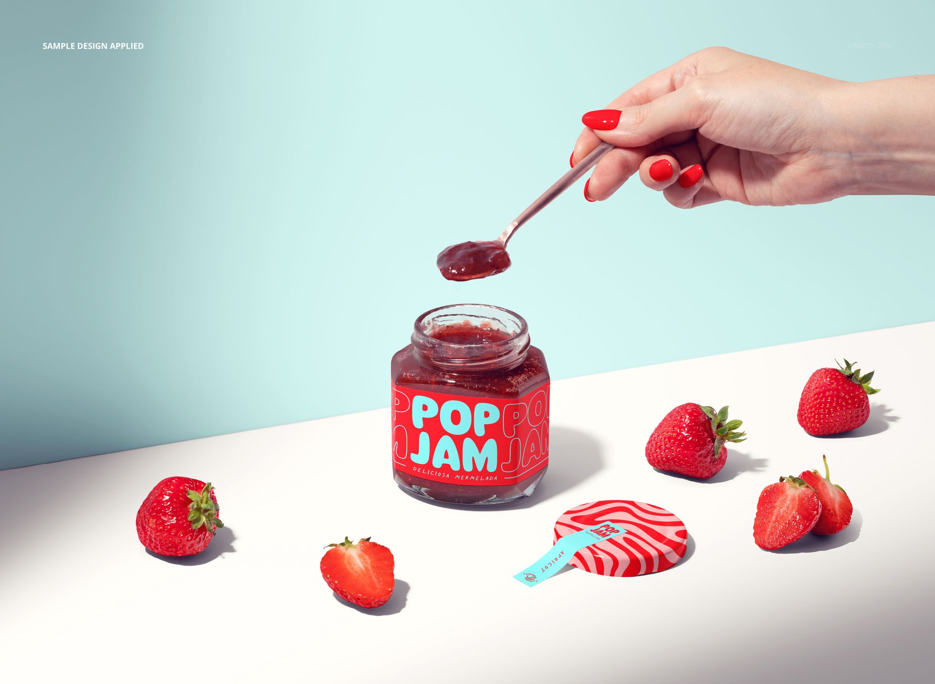Strawberry jam jar mockup with a bright label, strawberries, and a hand holding a spoon against a light blue background.