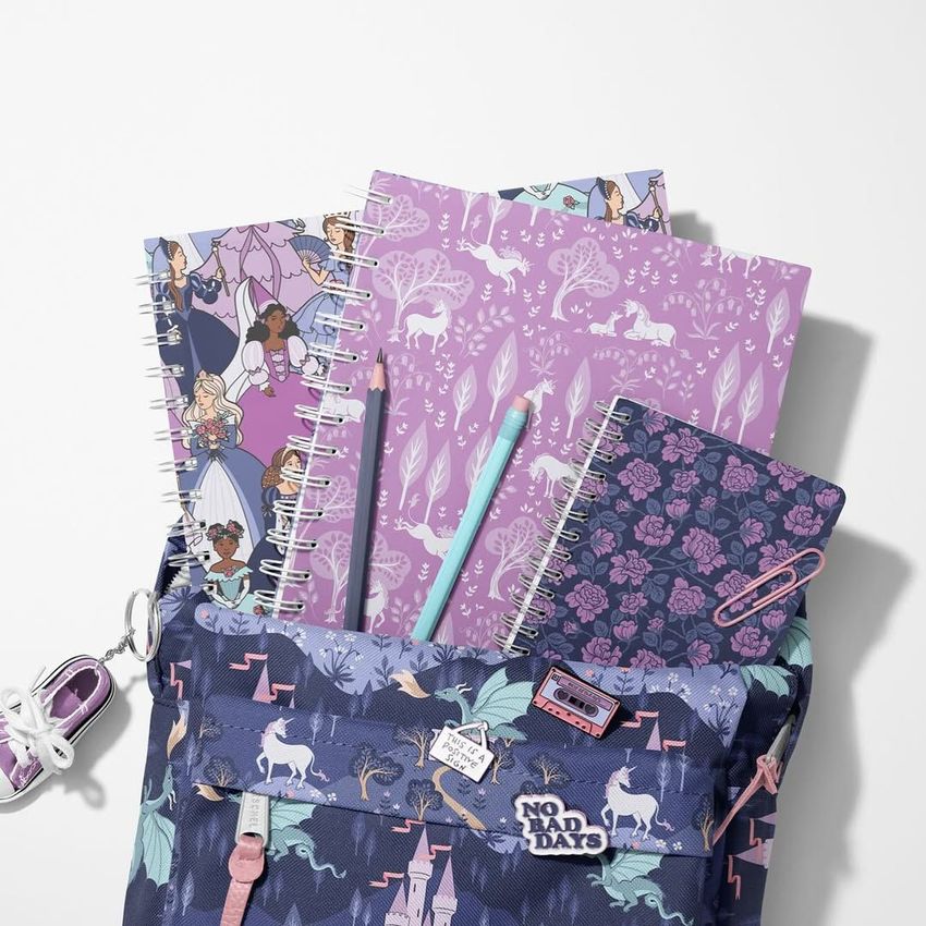 School backpack mockup with spiral notebooks featuring unicorn and garden patterns, shown from above on a light surface.