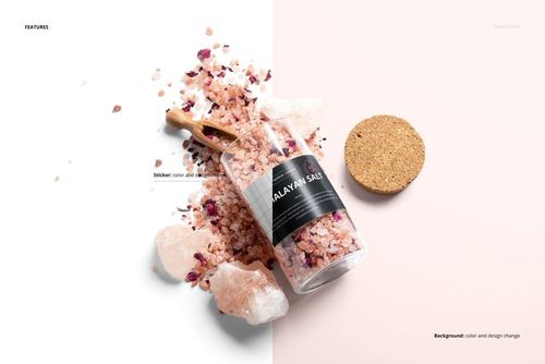 Glass jar of bath salts with a black label mockup, surrounded by pink salt crystals and a wooden scoop, top view.