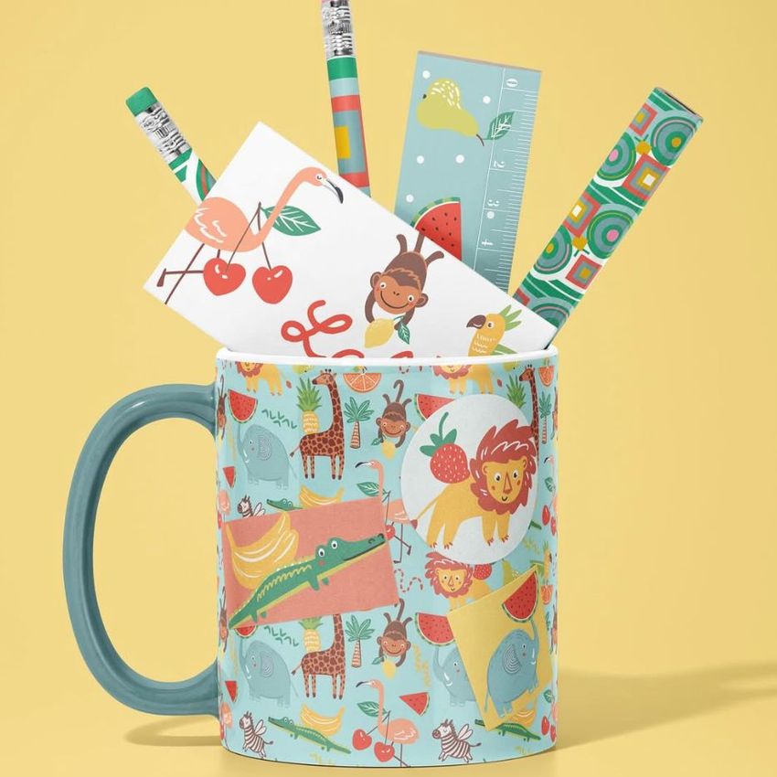 Mug mockup with a colorful animal pattern, filled with stationery items like pencils, pens, a ruler, and illustrated cards on a yellow background.