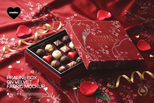 PSD mockup of an open praline box featuring various chocolates, set on patterned red velvet cloth with rose petals.