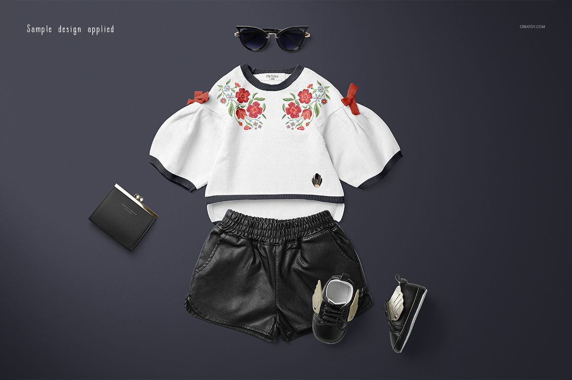 Kids sweater mockup featuring a white top with floral design, black shorts, shoes, and wallet on a dark background.
