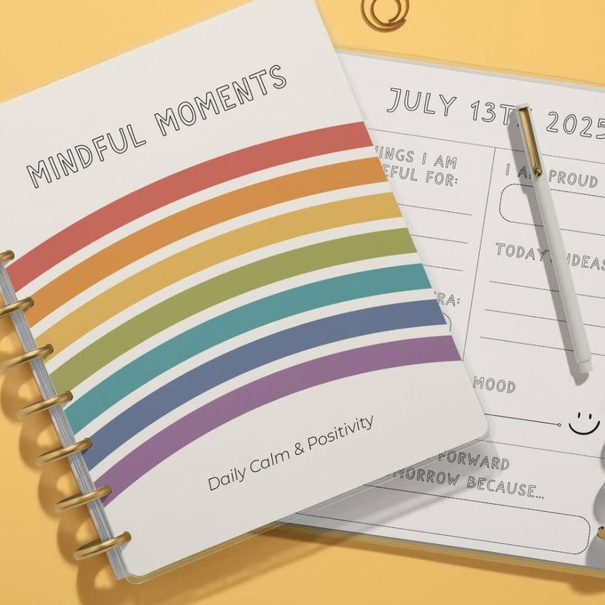 Top view of two spiral planners on a light surface, one closed with a rainbow cover and one open showing a daily planning page.
