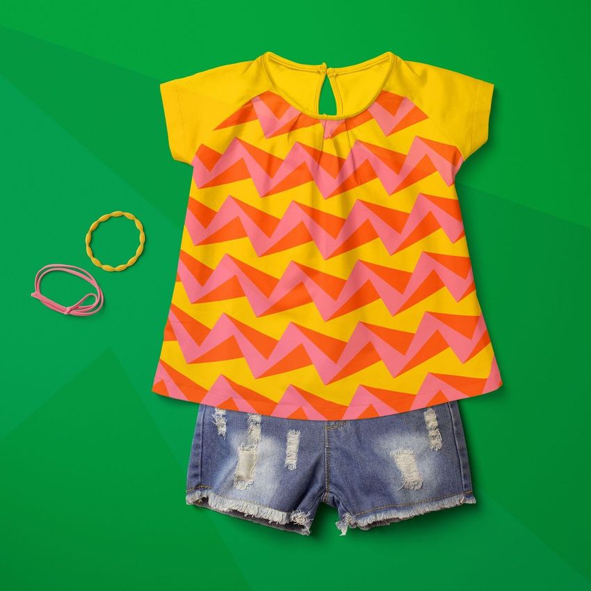 Kids summer set mockup featuring a yellow and pink zigzag patterned shirt paired with distressed denim shorts on a green background.