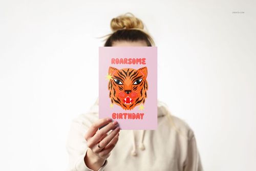 A5 card mockup held upright against a white background, featuring a pink card with a tiger illustration and birthday text.