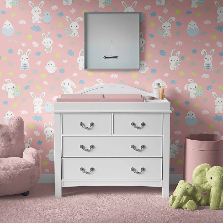 Baby room changing pad mockup featuring a white dresser with a pink pad, pastel bunny wallpaper, and plush toys on a pink carpet.