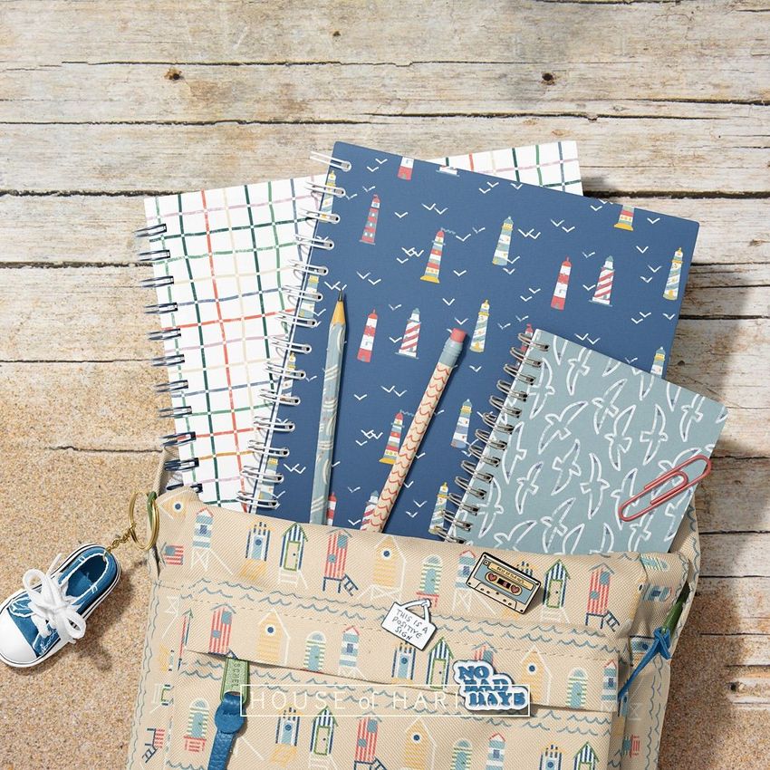 School backpack mockup with spiral notebooks in nautical patterns, pencils, and a small sneaker prop on a wooden surface.