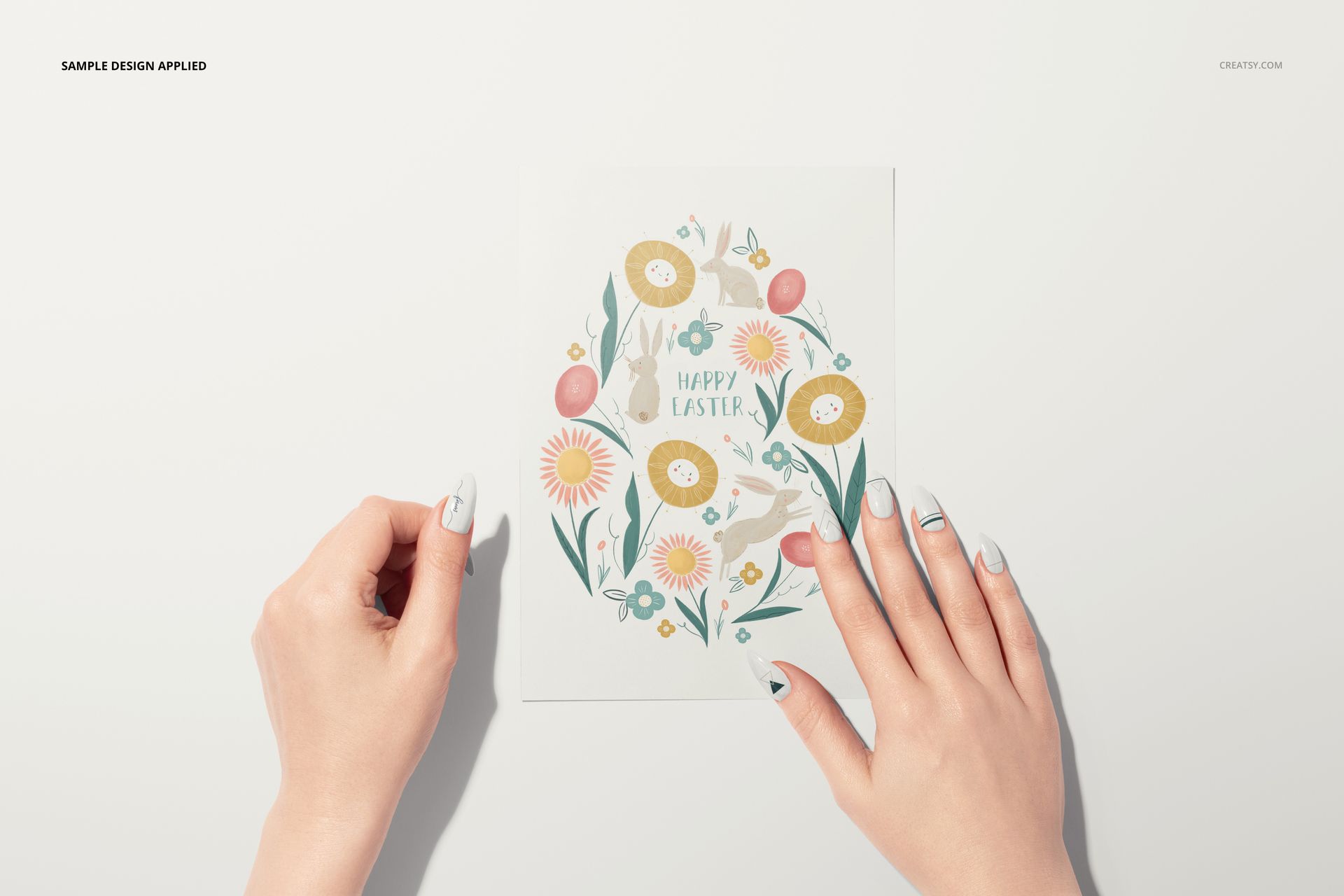 Greeting card mockup featuring a floral Easter egg design, shown from a top view with two women's hands holding the card.