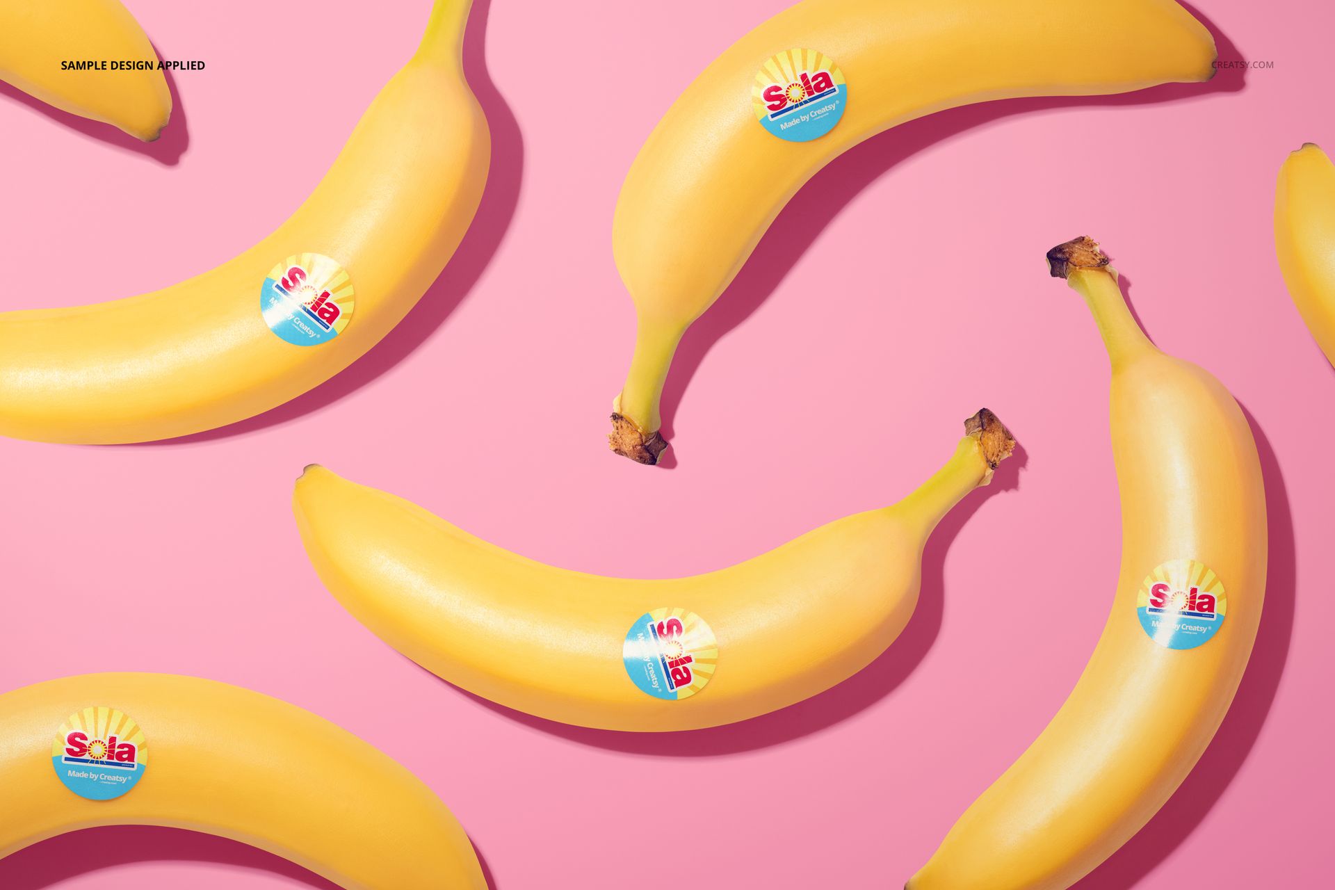 Top view of multiple bananas featuring round stickers, arranged on a vibrant pink surface for a mockup scene.