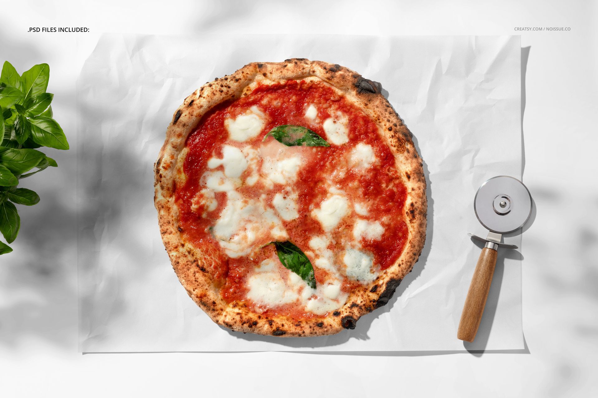Pizza mockup scene featuring a round pizza with melted cheese and basil, placed on white paper with kitchen props.
