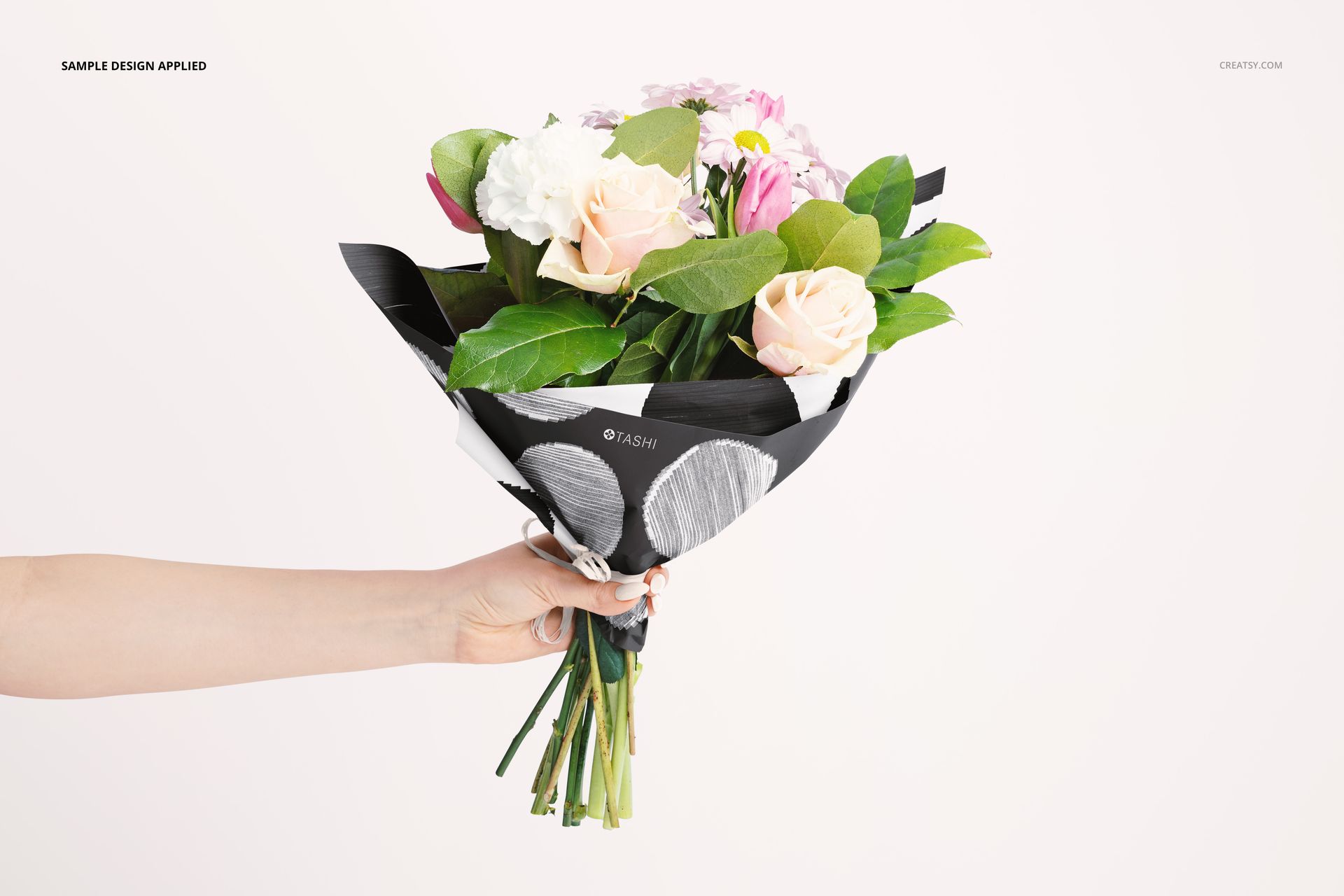 PSD mockup of flower packaging with a hand holding a bouquet, highlighting wrapping paper design and fresh blooms.