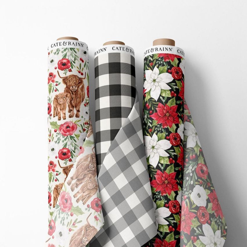 Fabric rolls mockup showing three upright rolls with Christmas-themed floral and plaid patterns on a white background.