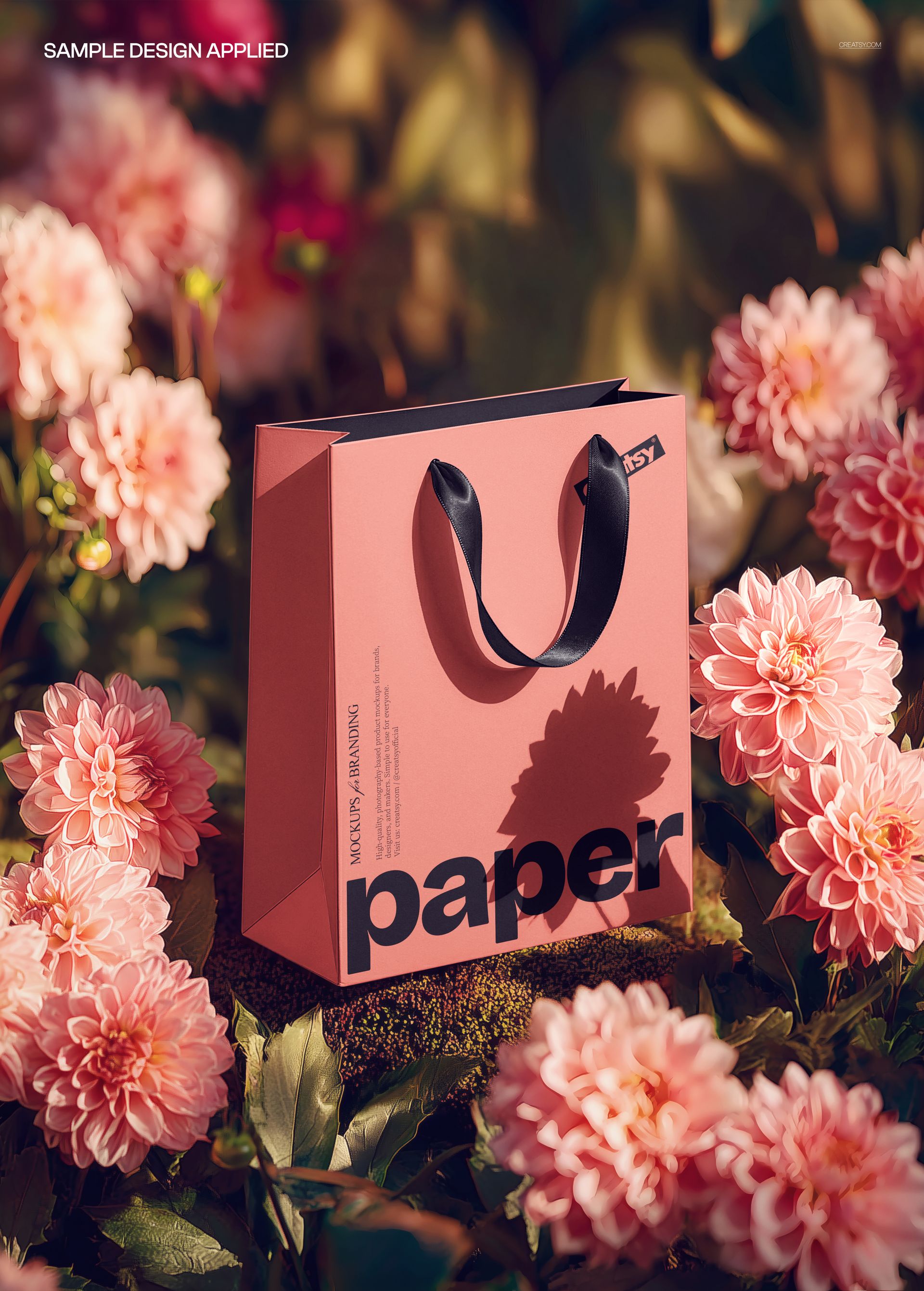 PSD mockup showing a pink paper shopping bag among lush pink flowers, with sunlight casting soft shadows.