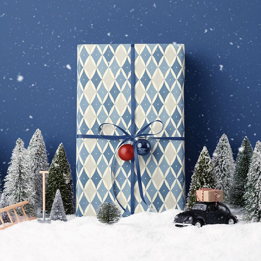 Christmas gift mockup featuring a blue and white patterned present with ribbon, set in snowy scenery with miniature trees and car.