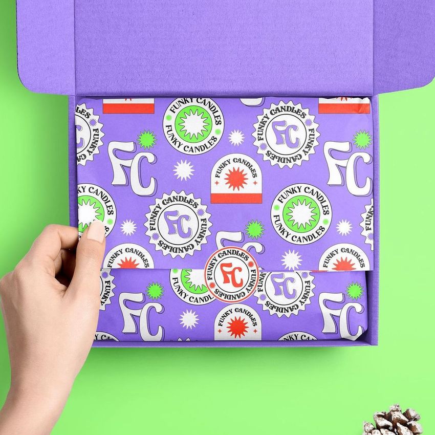 Mailer box mockup with purple wrapping tissue paper featuring bold graphic patterns and logos, shown on a green background.