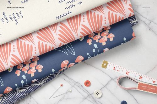 PSD mockup showing stacked patterned cotton fabrics in blue and cream beside a measuring tape and sewing tools on marble.