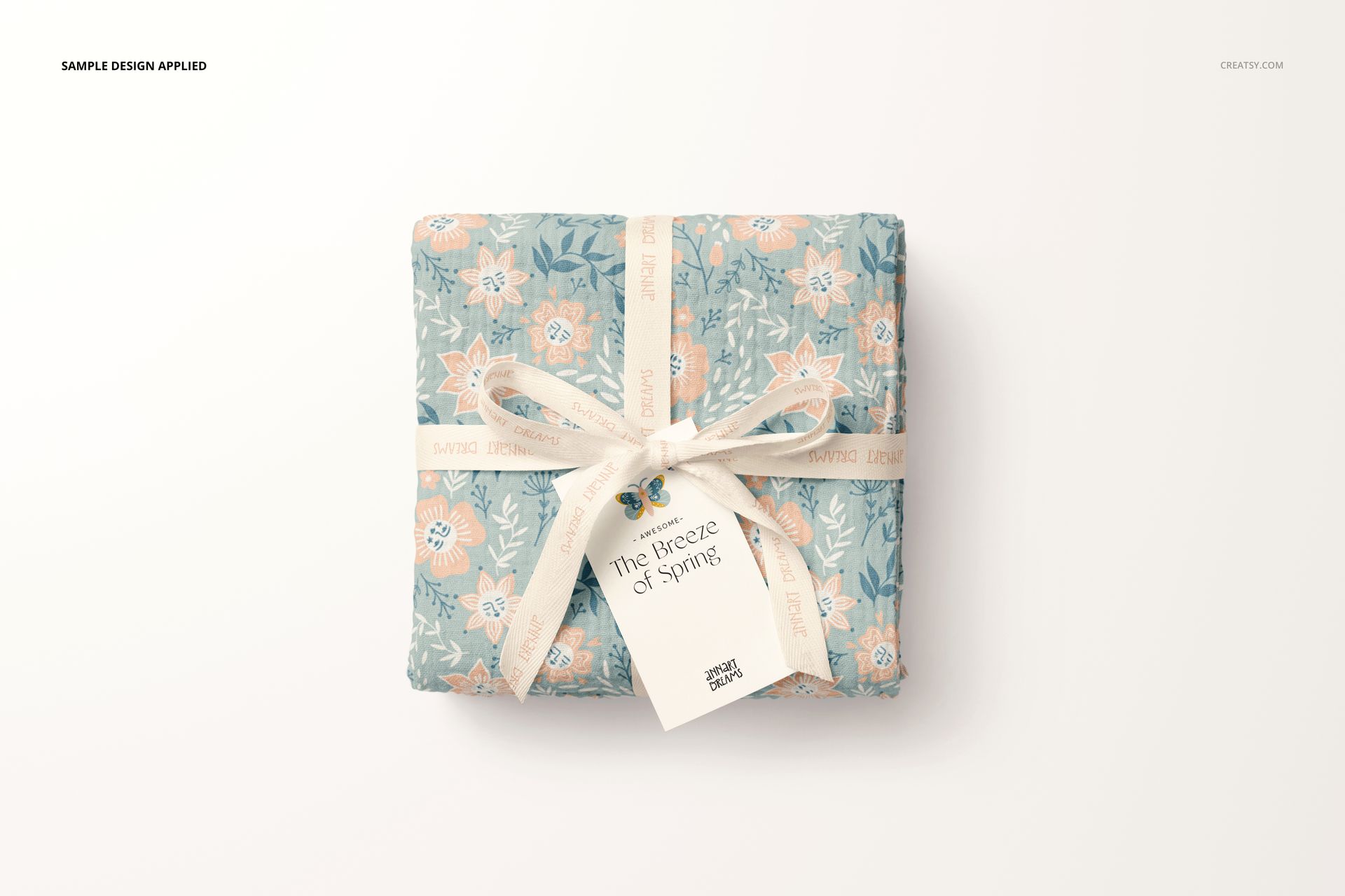 Top view of a crinkle muslin swaddle blanket mockup featuring a soft blue and peach floral design, wrapped with ribbon.