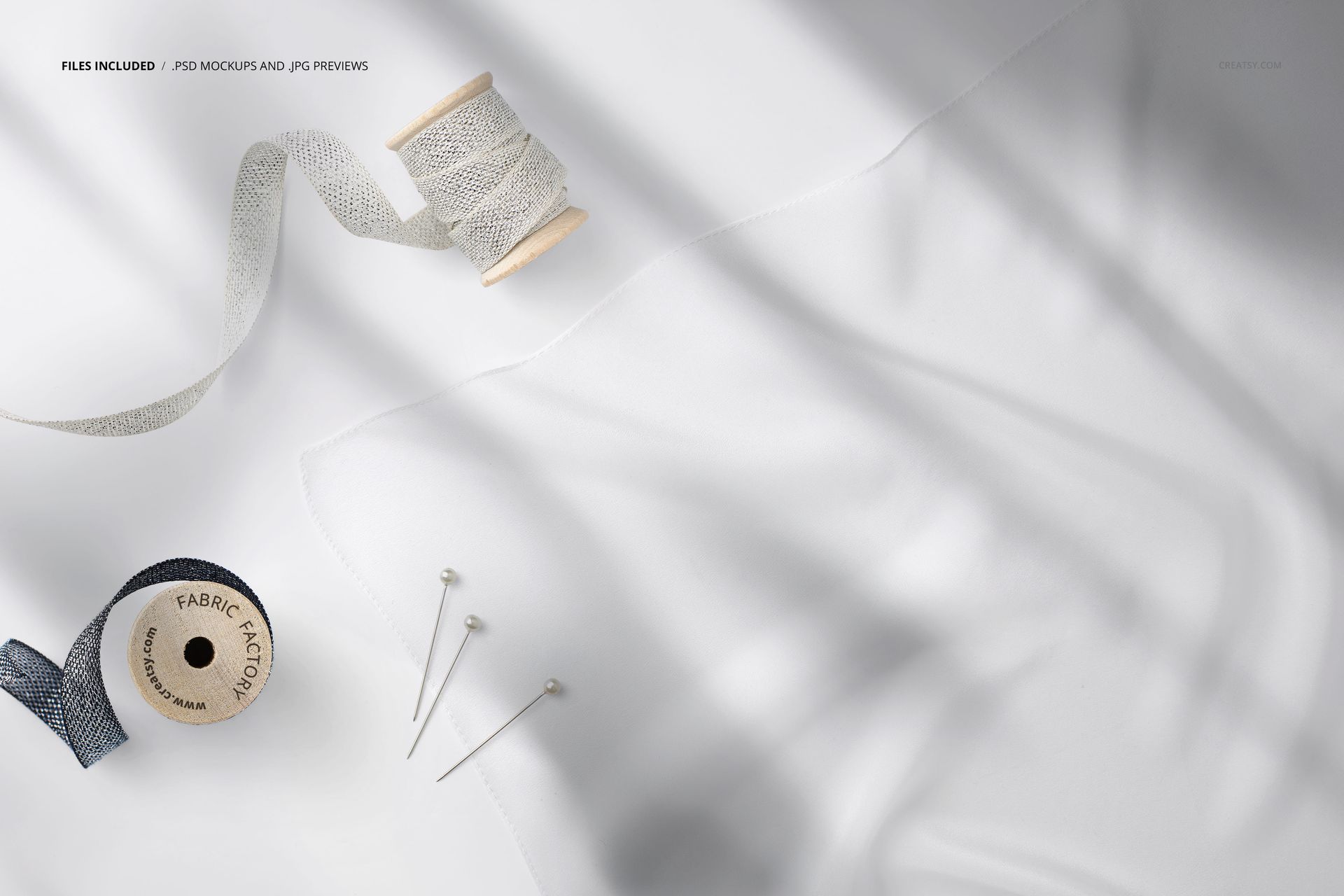 Close-up view of a square silk scarf mockup with two spools of ribbon and sewing pins on a light surface.