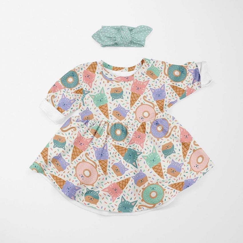 Baby jersey dress mockup with a playful pattern of cartoon cats in ice cream cones and donuts, paired with a green headband on a white background.