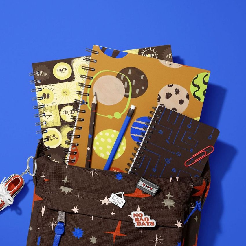 School backpack mockup with spiral notebooks in playful outer space and geometric patterns, shot from above on a blue background.