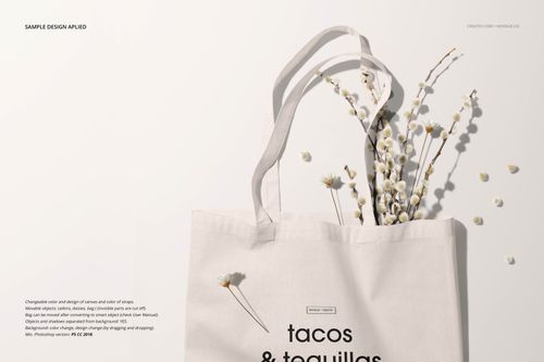 Front view of a light beige tote bag mockup with black text design, styled with dried white flowers on a neutral background.