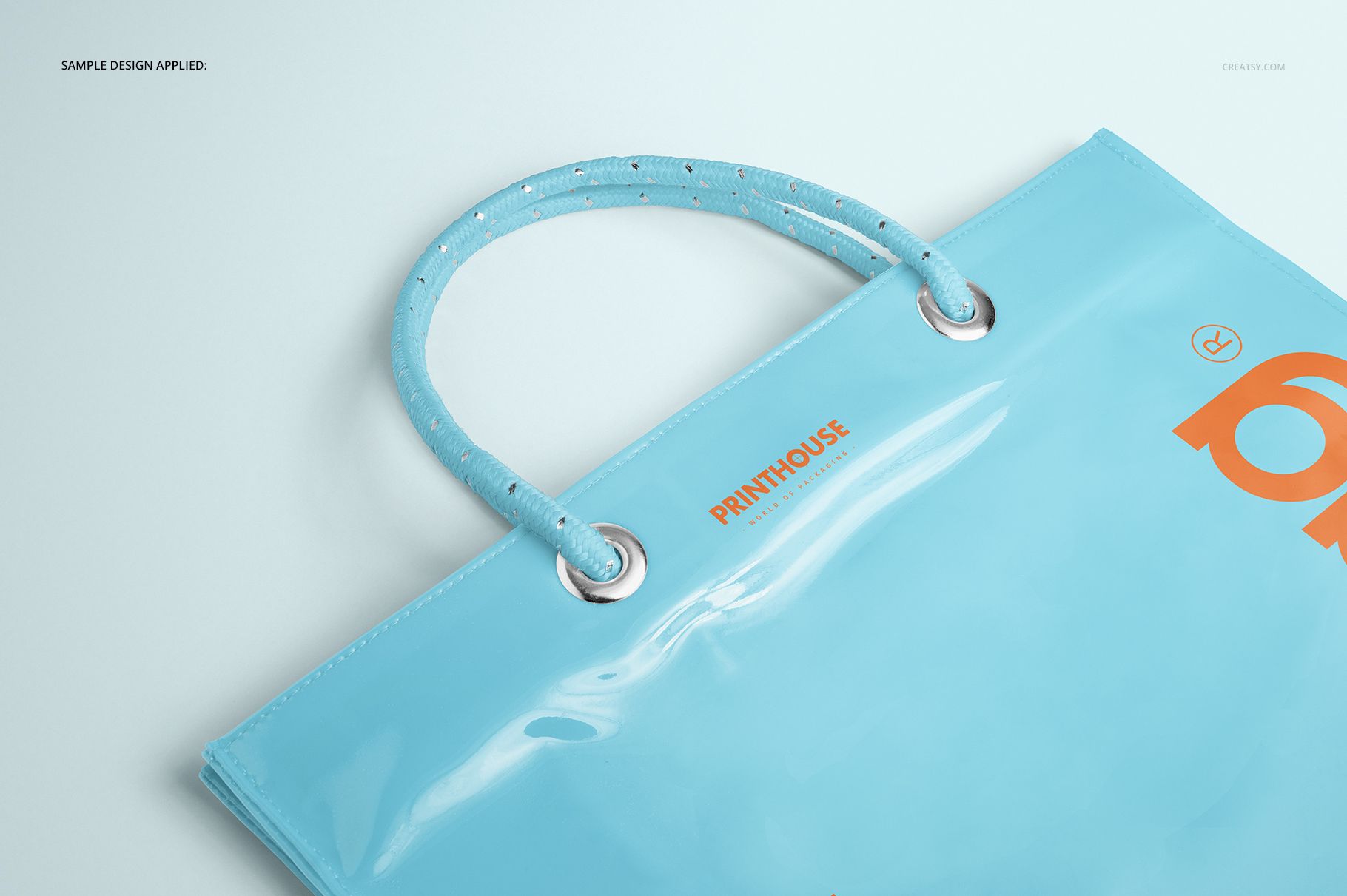 Glossy light blue vinyl PVC tote bag mockup featuring sturdy handles and metallic grommets, photographed from above.