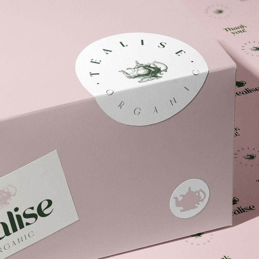 Sticker mockup featuring round and rectangular labels with green text and teapot illustration on a pale pink box.