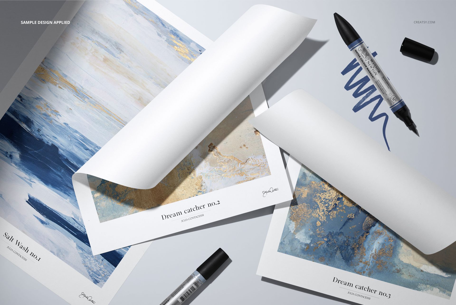 PSD mockup featuring two folded paper sheets displaying abstract designs, with markers and a blue scribble nearby.