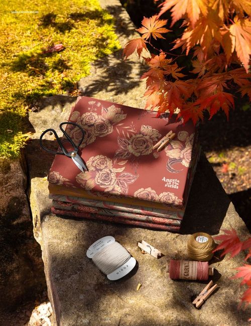 PSD mockup showing patterned fabric squares on a mossy stone ledge, accented by sewing supplies and orange maple leaves.