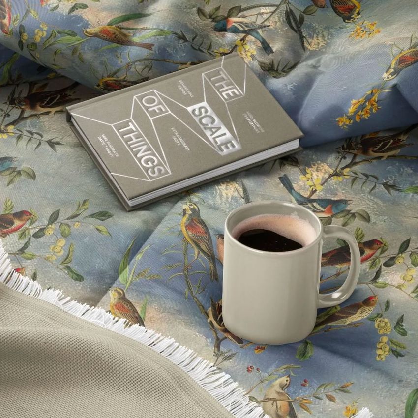 Microfiber comforter mockup featuring a botanical and bird print, with a ceramic mug and two stacked books on top.