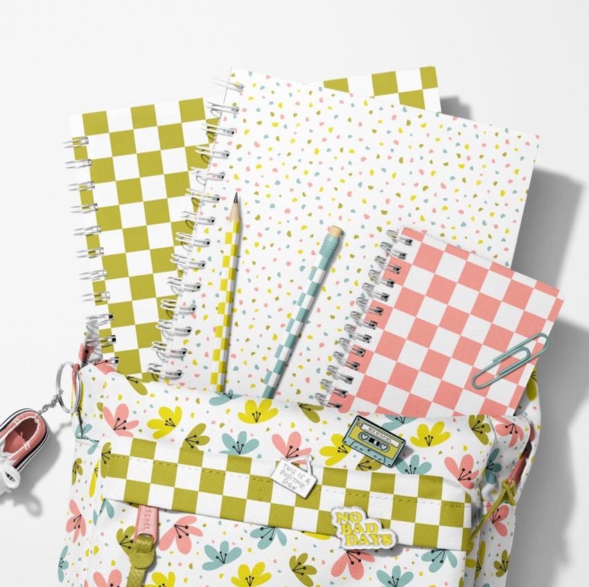 School backpack mockup with spiral notebooks featuring checkered and confetti patterns, pencils, and a paperclip on a white background.