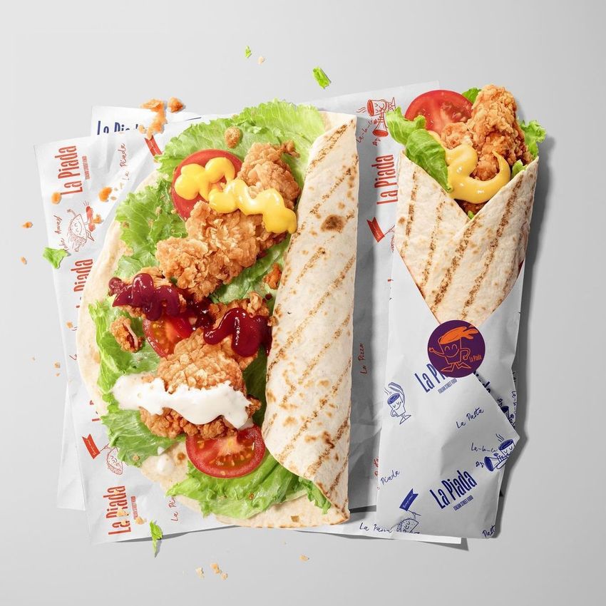 Food safe paper mockup featuring two tortillas with fried chicken, lettuce, tomato, and sauces, shown on branded wrapping paper.