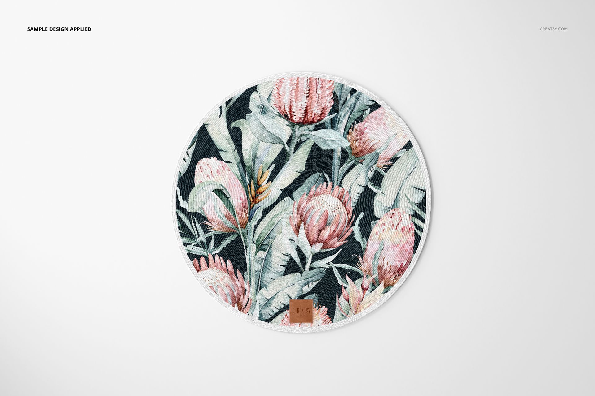 Top view of a round knitted rug mockup displaying a floral design with pink flowers and green foliage on a white surface.