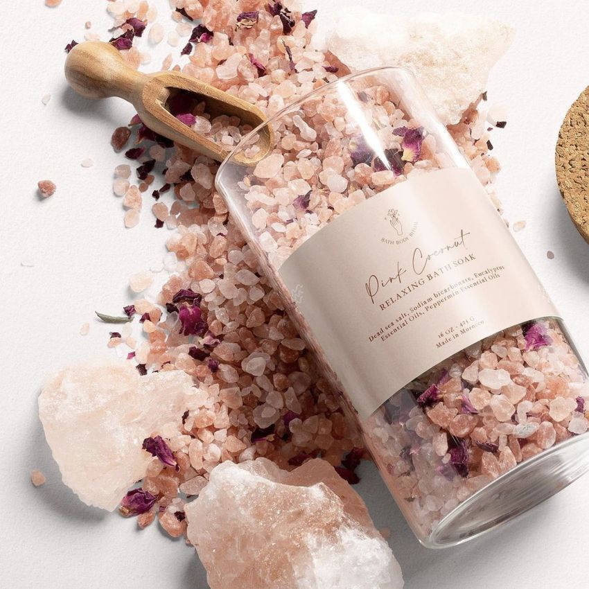 Close-up of a packaging mockup showing a labeled glass jar of pink bath salts with a wooden scoop and loose salt on a light background.
