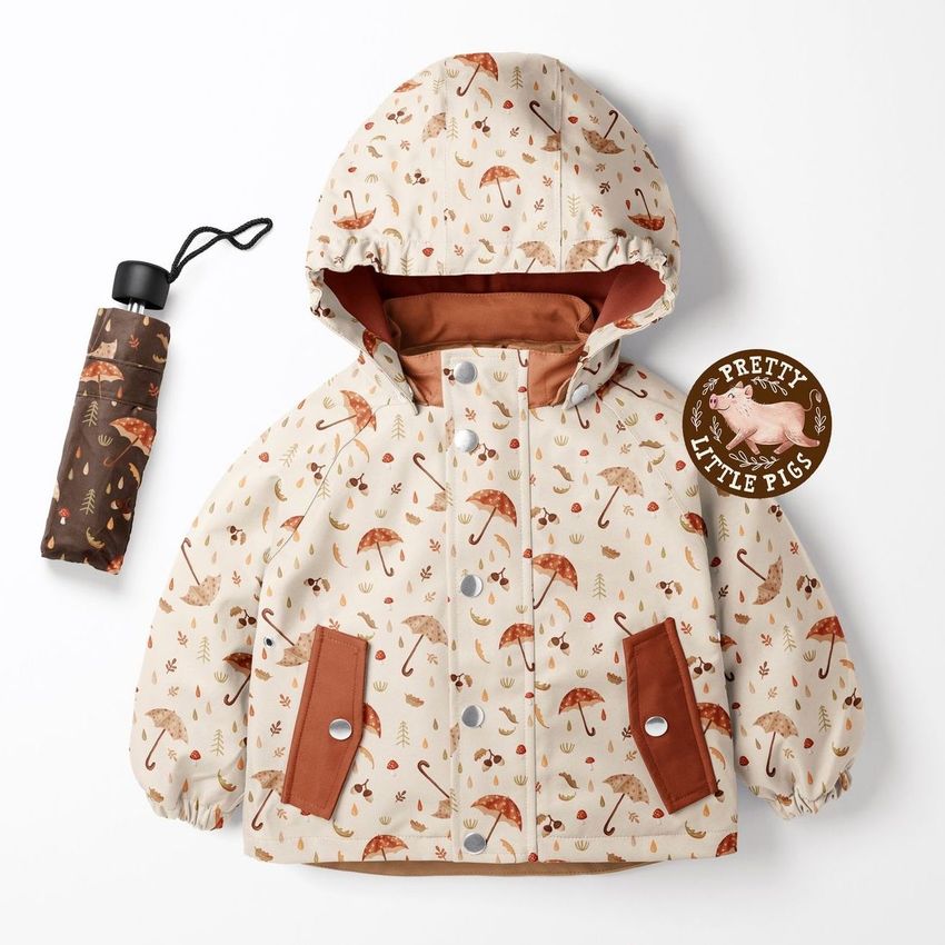 Kids rainwear mockup featuring a hooded jacket with autumn umbrella patterns, a brown umbrella, and a round badge on a white background.