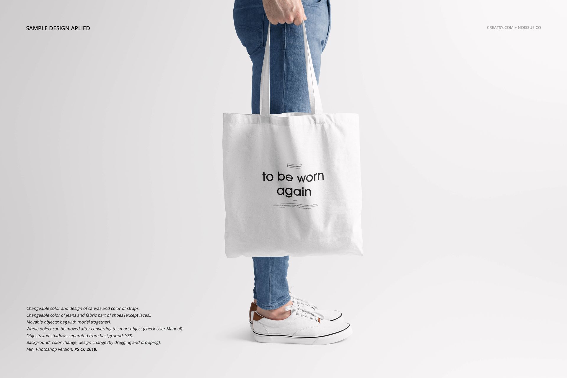 Front view of a white tote bag mockup held by a person wearing blue jeans and white sneakers against a plain background.