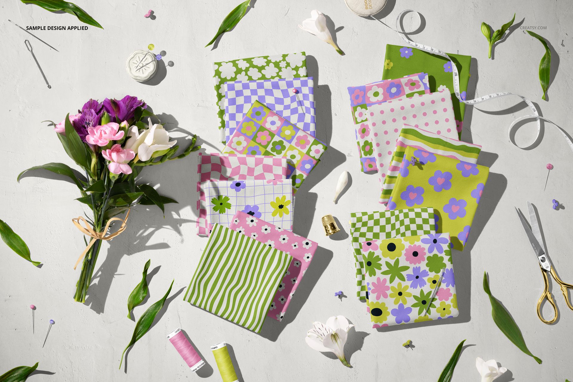 Assorted jersey fabric mockup samples with colorful flower and leaf designs, arranged with sewing tools and fresh flowers.