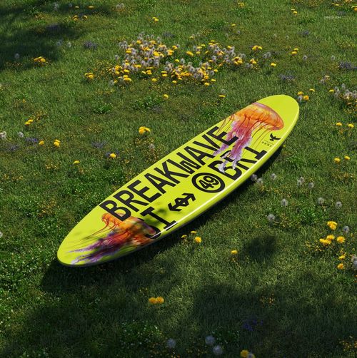 Surfboard longboard mockup featuring a vibrant yellow board with graphic text, placed on a grassy field.