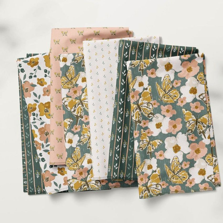 Folded fabrics mockup featuring a variety of floral and butterfly patterns in green, pink, white, and yellow tones on a light background.