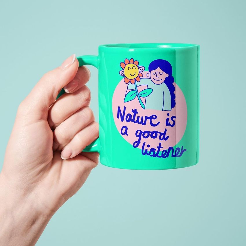 Hand holding a custom mug mockup with a turquoise background, featuring a colorful illustration and readable text on the mug.